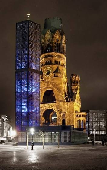 Berlin's Kaiser Wilhelm Memorial Church at night: the ruined tower lit gold beside the modern blue-glass bell tower